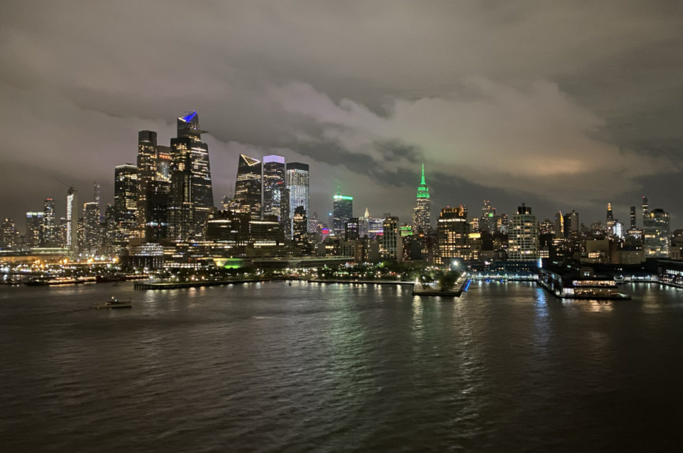 New York City Skyline is lit up under cloudy skies with the Empire State Building lit up green